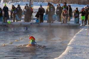 A crowd stands on ice by open water divided into lanes and watches swimmers