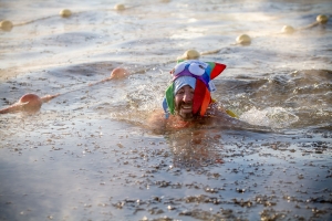 Adriano Bonforti, wearing a colorful squid hat with a logo that says IceLab on it, swims through water filled with small pieces of ice
